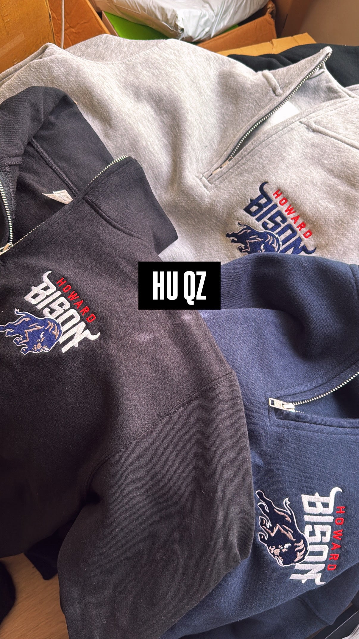 Three hoodies with logos and text, including 'Howard Bison QZ', on a wooden surface.